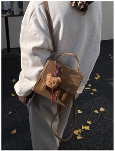 Brown leather backpack crossbody bag with a cute bear charm shown in a street scene