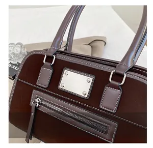 Détail d'un sac à main en daim marron foncé avec surpiqûres blanches et plaque métallique