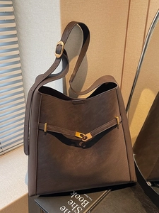 Large dark brown leather tote bag with gold buckle detail in a minimalist interior setting