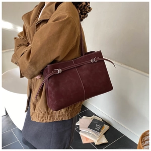 Macro detail of wine red suede tote bag with contrast stitching and metal buckle accents