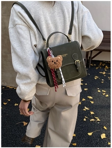 Dark green leather backpack with cute plush bear charm in an autumn street setting