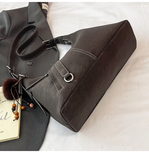 Detail of dark coffee shoulder bag featuring white contrast stitching and plush charm