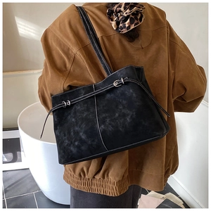 Detail of black suede tote bag showing contrast white stitching and metal buckle strap