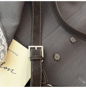 Close-up of brown litchi grain leather belt with silver buckle and white contrast stitching