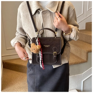 Detail of dark brown leather bag with white stitching, gold logo and a cute bear charm