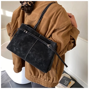 Detail of black suede tote bag with white contrast stitching and decorative belt strap