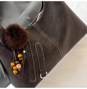 Close-up of deep brown tote with white stitching and plush ball decorative tassel