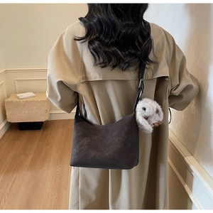 Detail of dark brown matte hobo bag with plush rabbit charm worn by model