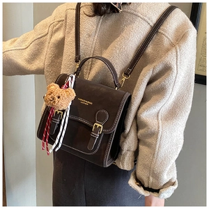 Detail view of brown retro backpack featuring white contrast stitching and plush bear charm