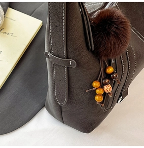 Detail of dark brown tote bag featuring white contrast stitching and a plush pompom charm