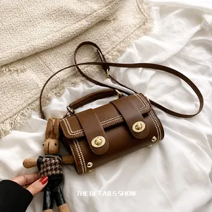 Detail van bruine leren tas met gouden dubbele draaisluitingen en kralenrand decoratie