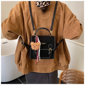 Detail of a retro black backpack with white stitching and a cute plush bear charm