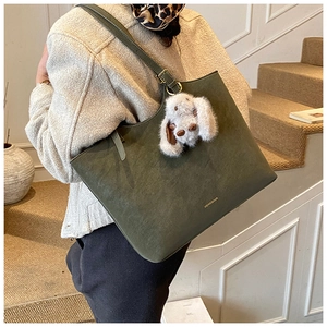 Detail of dark green matte tote bag with shoulder strap and plush rabbit pendant charm