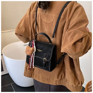 Close-up of black leather bag featuring white contrast stitching and cute bear charm