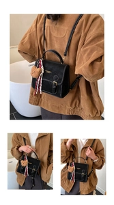 Detail of vintage black leather backpack with white stitching and bear charm
