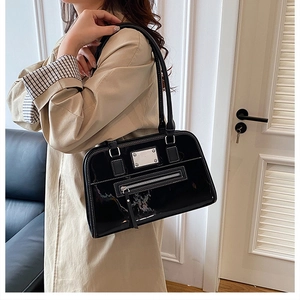 Détail d'un sac cabas en cuir verni noir avec plaque métallique sur un trench-coat beige