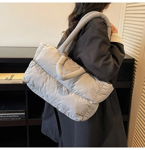 Detailed side view of light gray quilted puffer tote bag worn over the shoulder