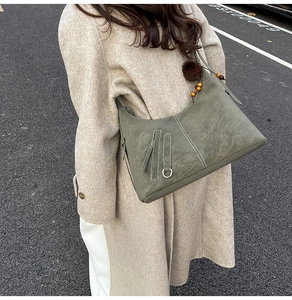 Detail of army green vintage hobo bag with furry pompom charm on a beige trench coat