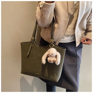Detail of olive green tote bag featuring adjustable straps and a plush rabbit charm accessory