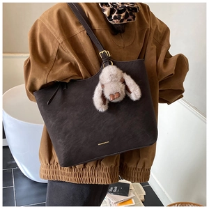 Large dark brown matte leather tote bag with plush bunny charm shown in a model lifestyle setting