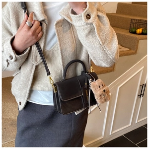 Detail of a black leather handbag with white contrast stitching and a plush dog charm