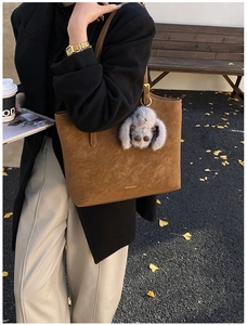 Detail of retro brown tote bag with fuzzy charm and gold logo in an autumn street setting