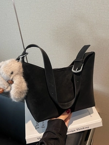Borsa a tracolla chic in camoscio nero con ciondolo a orsetto su sfondo di libro
