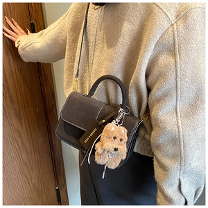 Details der dunkelgrauen Wildledertasche mit weißen Nähten und Plüsch-Hundeanhänger
