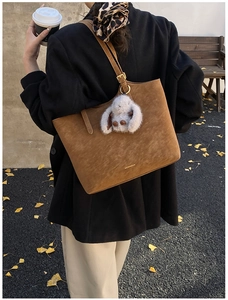 Brown suede tote bag with plush rabbit pendant and logo detail in autumn scenery