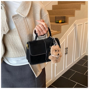 Details einer schwarzen Handtasche aus Leder mit weißen Nähten und Welpen-Anhänger