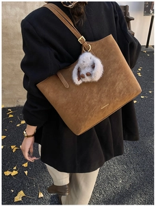 Detail of a brown suede tote bag with a gold logo and a cute white plush bunny charm