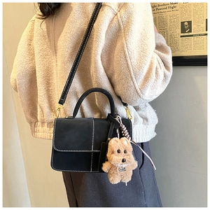 Detail of black matte crossbody bag with white stitching and brown plush bear charm