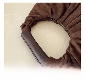 Detail of soft brown suede pleats and smooth leather handle of the minimalist cloud bag
