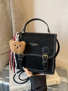 Retro black leather backpack with contrast stitching and plush bear charm on a suitcase
