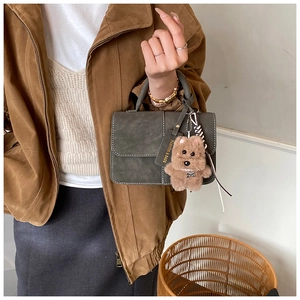Details der dunkeloliven Lederhandtasche mit Kontrastnaht und Plüschhund-Anhänger