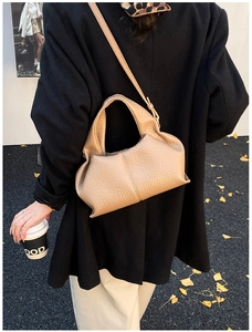 Détail du sac bandoulière beige en cuir texturé litchi porté avec un manteau noir et des feuilles