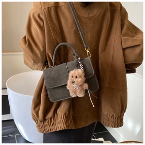 Detail of dark gray-green suede handbag with contrast stitching and teddy bear charm