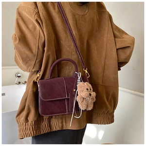 Detail of burgundy suede tote with white contrast stitching and cute puppy pendant