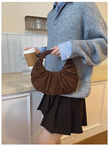 Close-up of pleated brown suede hobo bag carried by model in a cozy aesthetic setting