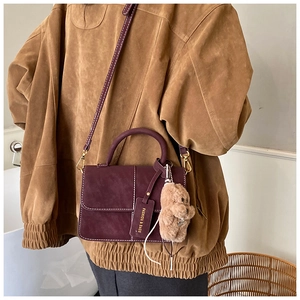 Detail der weinroten Handtasche aus mattem Leder mit Kontrastnaht und Bären-Anhänger