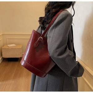 Deep red patent leather bucket bag with adjustable metal buckle strap shown on shoulder