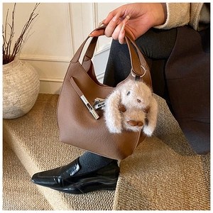 Detail of brown lychee grain leather bucket bag featuring a cute plush bunny charm