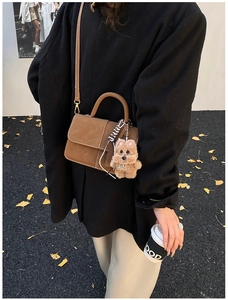 Detail einer braunen Wildleder Mini-Umhängetasche mit Plüschhund-Anhänger und weißer Naht