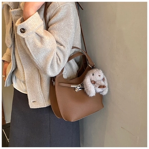 Detail of brown leather handbag with silver lock and plush bunny charm on a model