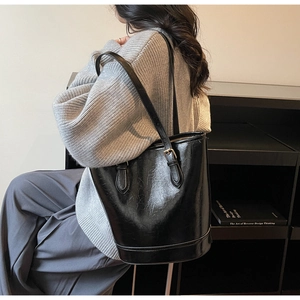 Side view of a glossy black bucket tote bag with adjustable strap on a female model