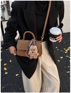 Braune matte Handtasche mit Plüschwelpen-Anhänger in einer herbstlichen Straßenszene
