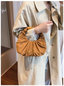 Detailed view of brown pleated crescent handbag with soft suede texture held by a model