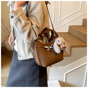 Detail of a brown leather shoulder bag with cross metal buckle and plush bunny charm