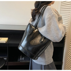 Detail of glossy black vintage tote bag with buckle decor on a woman shoulder