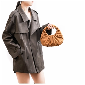 Detail view of brown pleated crescent handbag paired with a charcoal double-breasted coat
